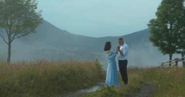 Adam, yoğun sis sırasında dağların ortasında dururken nazikçe kadının ellerini öpüyor..