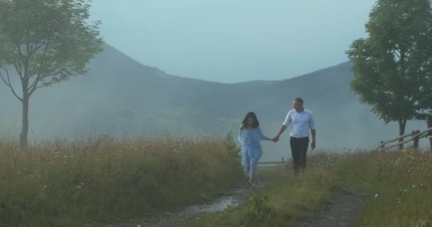 Šťastný milující pár se drží za ruce a kráčí po stezce v horách. Muž jemně objímá ženu v husté mlze.. — Stock video