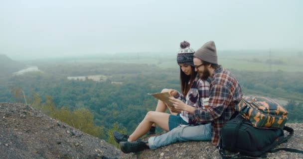 เดินทางไปภูเขา คู่นักสะกดจิตสาวที่มีเสน่ห์นั่งบนหินที่ปกคลุมด้วยหมอกหนาและเรียนรู้แผนที่ — วีดีโอสต็อก
