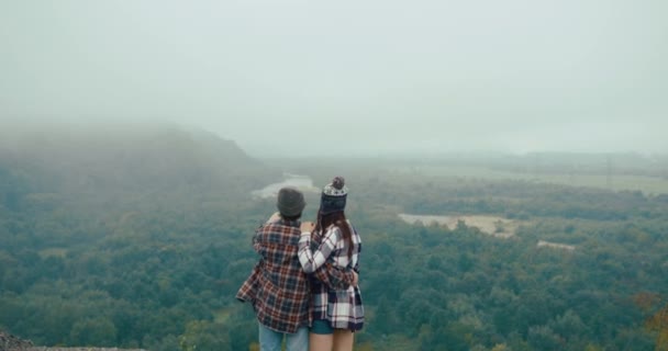 Perjalanan ke pegunungan. Pria dan wanita berpakaian hypster melihat pemandangan gunung dari batu tertutup kabut dan mengangkat tangan mereka ke atas loke pemenang — Stok Video