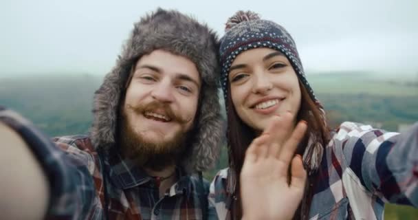 Pasangan muda hypster mengambil video dari diri mereka sendiri berdiri di atas batu dengan pemandangan gunung yang indah di belakang — Stok Video