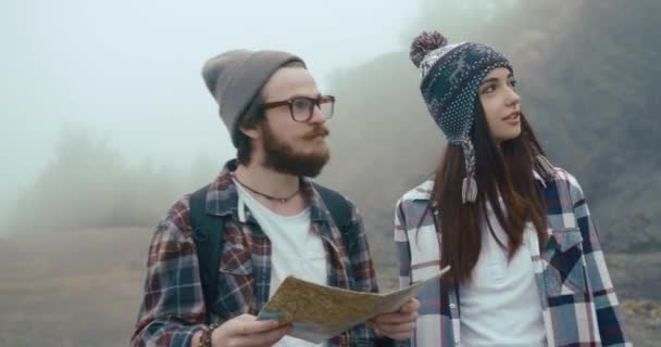 Călătoreşte în munţi. Băiat și fată îmbrăcat ca hipsterii plimbare cu harta în jurul munților acoperite cu ceață groasă — Videoclip de stoc