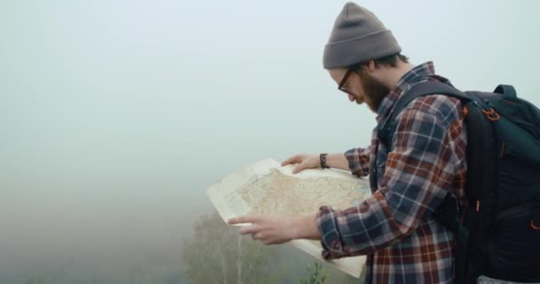 Viajar nas montanhas. Jovem com barba elegante aprende um mapa antigo andando na montanha coberto com nevoeiro espesso — Vídeo de Stock