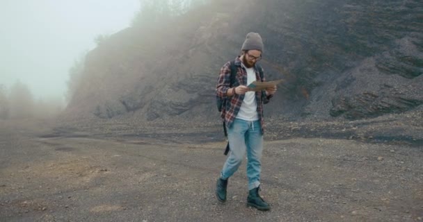 Bepergian di pegunungan. Anak muda dengan jenggot bergaya belajar peta tua berjalan di gunung ditutupi dengan kabut tebal — Stok Video