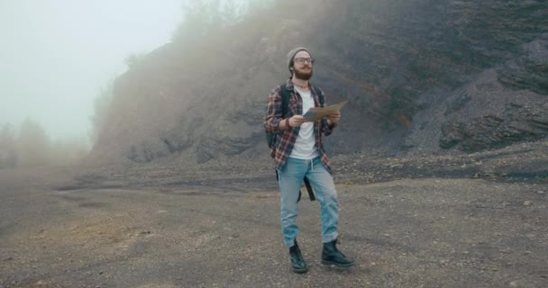 Bepergian di pegunungan. Anak muda dengan jenggot bergaya belajar peta tua berjalan di gunung ditutupi dengan kabut tebal — Stok Video