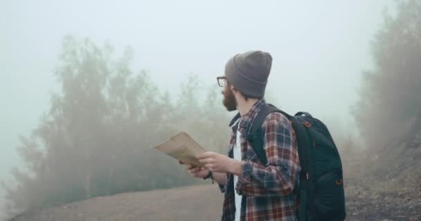 Bepergian di pegunungan. Anak muda dengan jenggot bergaya belajar peta tua berjalan di gunung ditutupi dengan kabut tebal — Stok Video