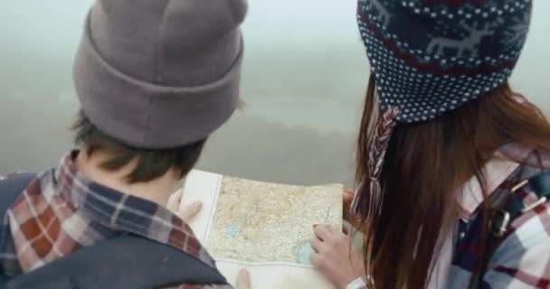 Matkusta vuorille. Poika ja tyttö pukeutunut hypsterit kävellä kartta ympäri vuoria peitetty paksu sumu — kuvapankkivideo