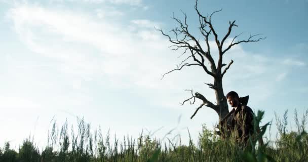 Um lenhador com um machado no ombro corre perto de uma árvore seca alta. Carvalho seco velho solitário. natureza segura. céu bonito — Vídeo de Stock