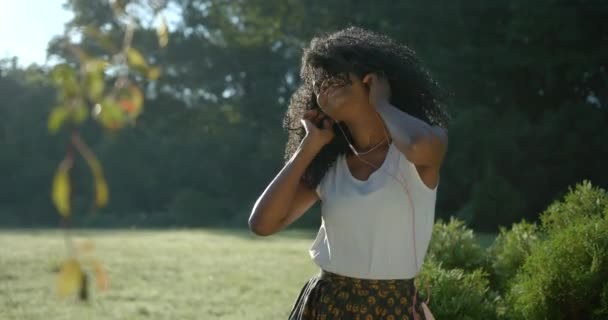 感情上漂亮的非洲裔美国女孩 有着绿色的眼影和可爱的微笑 正在欣赏耳机里的音乐 她在花园里精力充沛地跳舞 — 图库视频影像