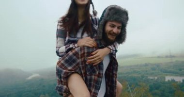 Kışlık şapkalı genç bir kız, arkasında güzel bir dağ manzarası olan kayanın üstünde yele omuzlarına atlıyor..