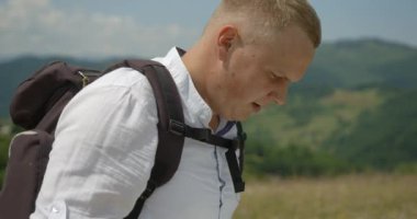 Close-up side portrait of the handsome happy blond man tourist with backpack checking the road with the paper map during hiking in mountains. 4k footage