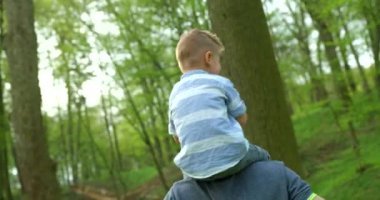 The handsome happy father is giving his little son the piggyback ride and spinning him round in the green forest. 4k footage