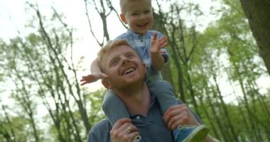 Father and son are having fun in the forest. The handsome man is giving his son the piggyback ride. Close-up portrait. 4k footage