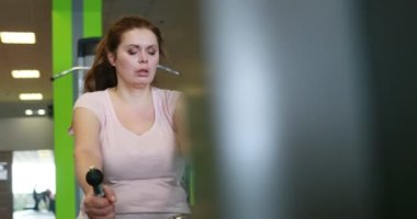 Portrait of the obese woman actively working out on the rowing machine in the green gym. Camera is moving left and right