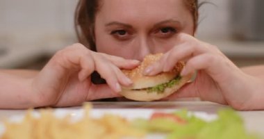 Close-up portrait of the obese woman eating the burger with pleasure. 4k