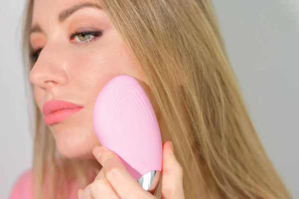 Genç kadın yüz masajı pembe fırçası kullanıyor.
