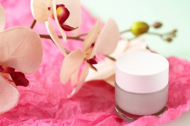 Cam kapta yeşil ışık kremi ve pembe arka planda orkide çiçekleri.