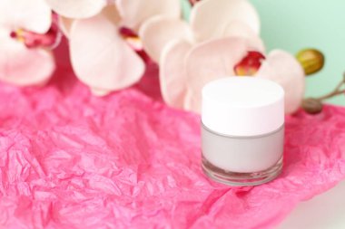 Cam kapta yeşil ışık kremi ve pembe arka planda orkide çiçekleri.