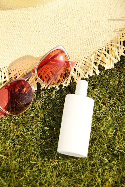 Sunscreen solar protection cream with sunglasses and straw hat on green grass, tropical sunny day