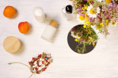 Kozmetik, ayna, çiçek ve meyve şişeleri ahşap masada.