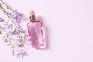 Pembe arka planda pembe parfüm şişesi ve doğal çiçekler.
