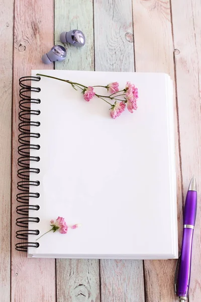 Blank white notepad page with flowers and pen on wooden table