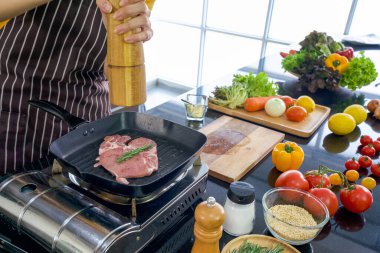 Şef bifteğe biber koyuyor. Modern bir mutfakta sabah atmosferi. Mutfak tezgahı çeşitli sebze ve baharatlarla dolu..