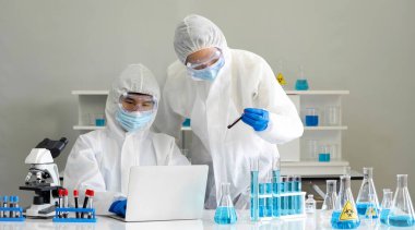 Virüse karşı koruyucu giysi araştırmacıları internetteki kimyasal bileşikleri araştırmak için dizüstü bilgisayar kullanıyorlar. Coronavirus hastalığı 2019 (COVID-19) bir laboratuvarda test süreci.