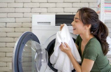 Asyalı ev hanımı çamaşır makinesinden yeni yıkanan beyaz bez kokusunu içine çekti. Çamaşır odasında çalışma ortamı.