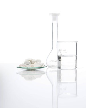 Close up chemical ingredient on white laboratory table. Calcium carbonate Chip in Chemical Watch Glass place next to beaker with alcohol and Volumetric flask. Side View clipart