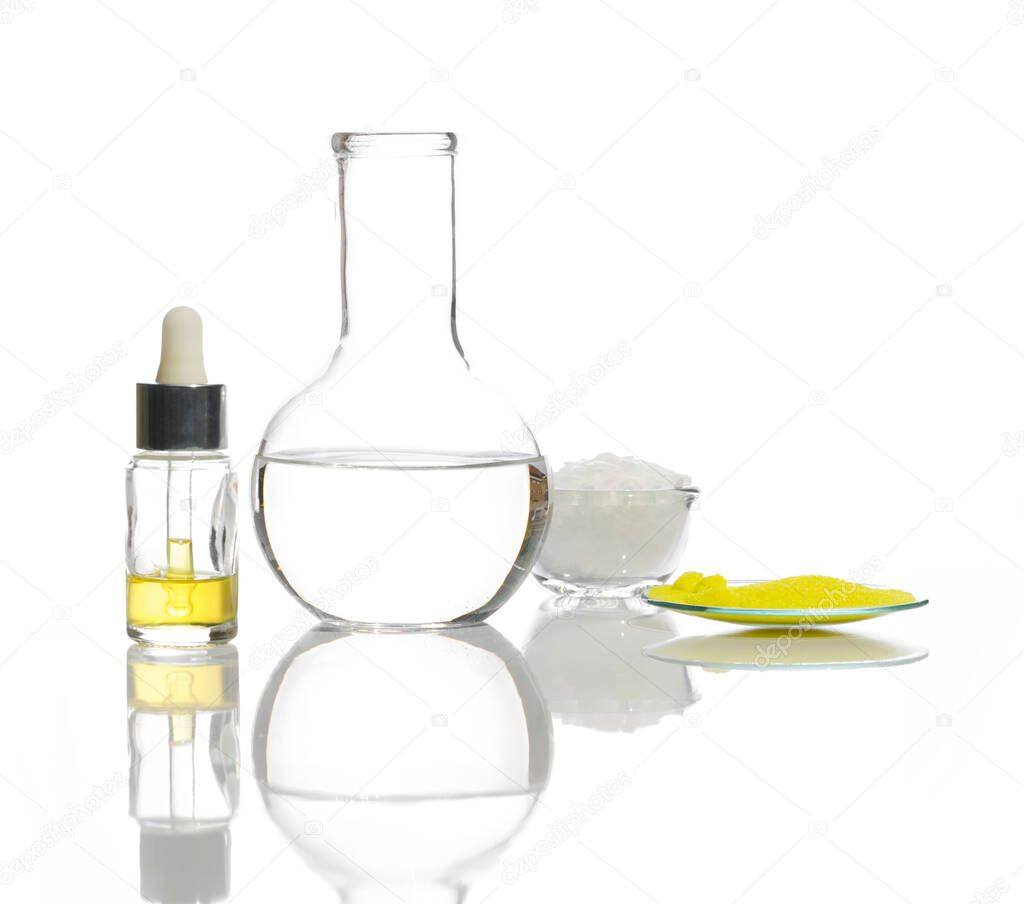 Closeup chemical ingredient on white laboratory table. Yellow cosmetic liquid in Dropper Bottle, Crystal clear liquid in Flat Bottom Flask, White flake chemical and Potassium Chromate powder.