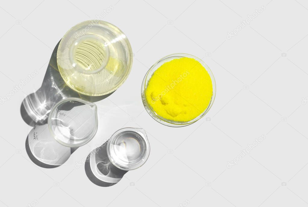 Closeup chemical ingredient on white laboratory table. Potassium Chromate powder in Chemical Watch Glass place next to beaker with alcohol and Erlenmeyer flask. Top View