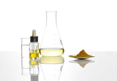 Damla şişesinde sarı kozmetik sıvısı, Erlenmeyer şişesinde Poli Alüminyum klorür sıvısı, deney masasında kristal berrak beher içinde sıvı ve kimyasal saat bardağında Organik Curcuma tozu..