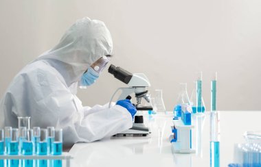 Virüse karşı koruyucu giysi üzerine epidemiyolojik araştırmacılar enfekte olmuş insanların kan örneklerine bakmak için mikroskop kullanıyorlar. Coronavirus hastalığı 2019, Omicron test süreci laboratuvarda.