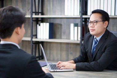 Asian manager in black suit interview the applicant with a smile. The atmosphere of job interview in the modern office.