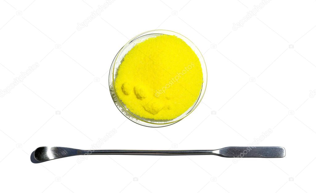 Closeup chemical ingredient on white laboratory table. Potassium Chromate powder in Chemical Watch Glass placed next to the stainless spatula. Top View