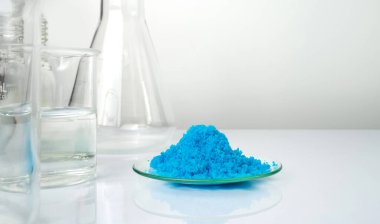 Beyaz laboratuvar masasında yakın çekim inorganik kimyasal. Kimyasal Saat Camındaki bakır (II) sülfat, Beaker 'daki alkol sıvısının yanına yerleştirildi. Kozmetik ve Tuvalet ürünleri için kimyasal malzeme.