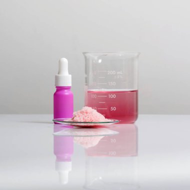 Beyaz laboratuvar masasında güzellik hizmetleri için kimyasallar. Kimyasal Saat Camı 'ndaki pembe pullu kimyasallar damlatıcılı Serum şişesinin yanında ve beher içinde kırmızı EPOXY sıvı rasin var.. 