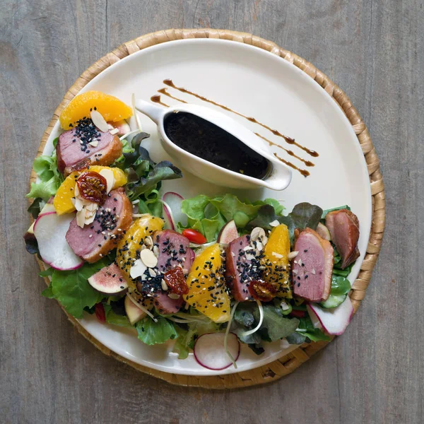 Smoked duck breast salad with brown sauce served on wooden table. Top View