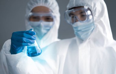 Covid-19 laboratuvarda test ediliyor. İki bilim adamı Erlenmeyer şişesinde mavi sıvı kimyasalı tartışıyor. Mavi ışık efekti. Sağlık ve Tıp Konsepti.