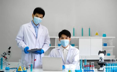 Laboratuvarda çalışan yüz maskeli ve cüppeli iki bilim adamı. Omicron test süreci, Coronavirus hastalığı 2019.