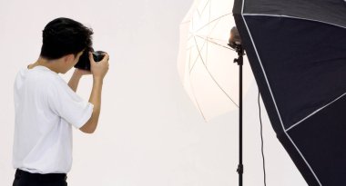 Asian photographer looks through the viewfinder while shooting with the camera. Working atmosphere in the photo studio.