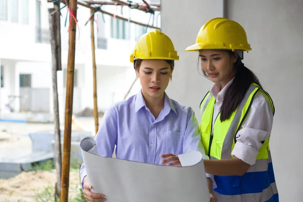 Young engineer in a construction helmet and safety vest explaining to project owner about a floor plan. Work environment of engineers at the construction site of housing projects.