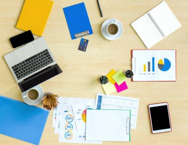 Ofisteki masanın yüksek açılı görüntüsü. Laptop bilgisayarı, tablet, cep telefonu, kredi kartı, kahve, kırtasiye, belge, grafik, tablo ahşap.