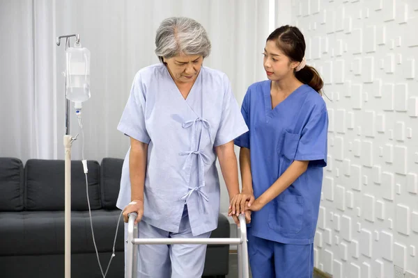 Young asian nurse at nursing home take care disabled senior woman. Caregiver doctor serve physical therapy for elderly patient to exercise and practice walking on walker or cane.
