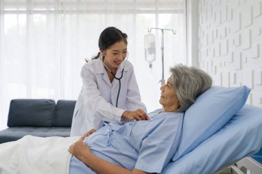 Kıdemli kadın hasta ve doktor. Genç Asyalı doktor yaşlı hastanın kalp atışlarını kontrol etmek için steteskop kullanıyor..