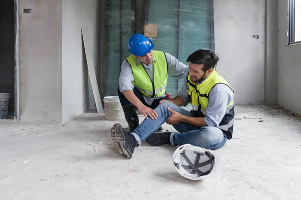 Güvenlik yelekli genç beyaz adam dizini tuttu ve acı içinde bağırdı. İnşaat alanındaki yaralar yüzünden. Asyalı arkadaşı geldi ve ayağa kalkmasına yardım etti..
