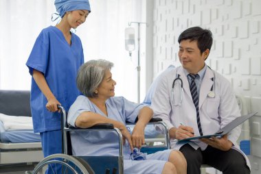 Young nurse push a wheelchair of the elderly patient while asian doctor with stethoscope and gown examine the symptom of the Total Knee Arthroplasty. Healthcare and medicine concept.