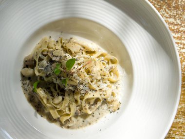 Tagliatelle Pasta with butter creamy white truffle sauce. Pasta with wild termite mushroom topped with truffle slice and watercress. Closeup italian food served on deep round plate. Top view