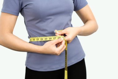 Closeup female hands in exercise clothes use a tape measure to measure around the waist. Healthy nutrition and weight losing concept. Portrait on white background with studio light.